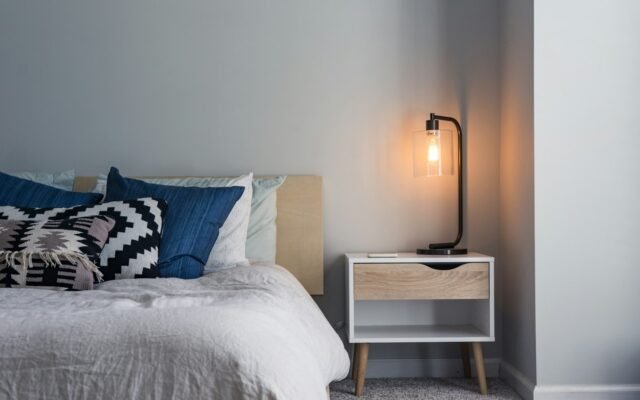 Black table lamp on a nightstand next to a bed